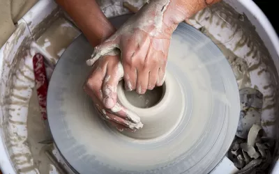 A pair of hands works on a clay pot on a pottery wheel.