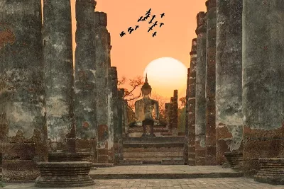 Sukhothai, Thailand at sunset with birds soaring over old temple pillars.
