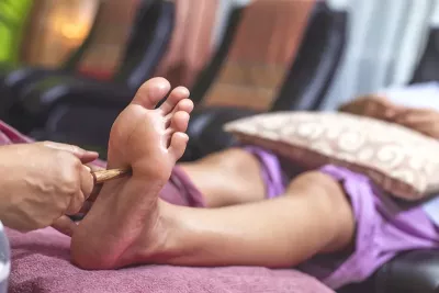 a practitioner using a Thai wooden stick on the foot of a person lying down.