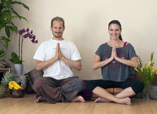 Heath and Nicole Reed, seated with crossed legs on the floor with hands in prayer position at their chests.