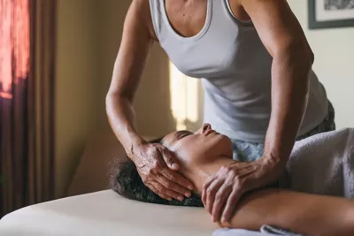 a massage therapist works on the neck area of a relaxed client with brown skin and hair.