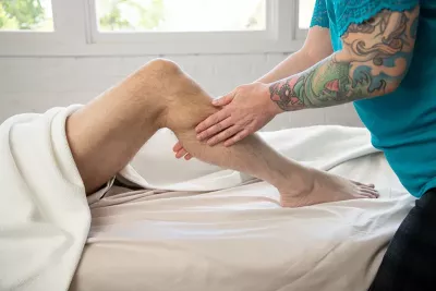 a massage therapist applying superficial rolling friction to a client's leg with both hands.