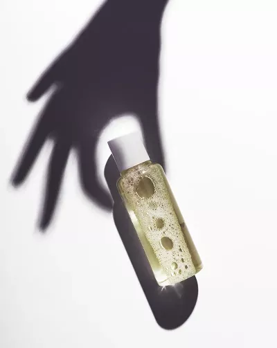 A shadow of a hand reaching for an unlabeled plastic bottle of oil.