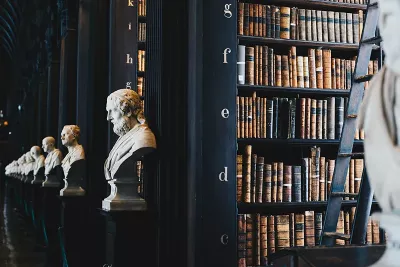 A large, dark library with rows of books and busts of historical figures.
