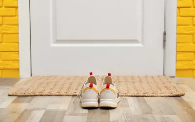 A pair of shoes sits in front of a door and welcome mat.