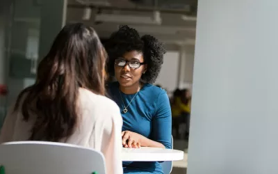 Two women at a table are seated talking.