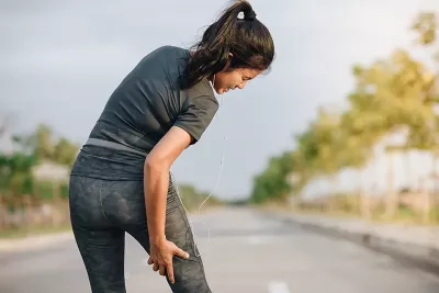 A woman grabs the back of her right leg which is causing her pain.