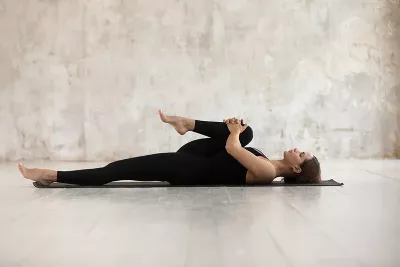 a woman lying on a yoga mat on her back stretches her right leg and glutes.