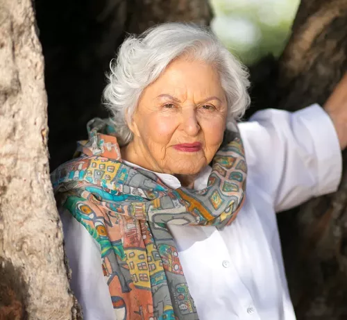 portrait of Deborah Szekely at nearly 100 years old, wearing a colorful scarf and white blouse.