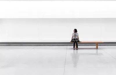 a woman sits on a long bench in an empty room.