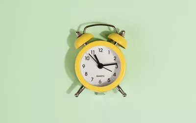 an analog alarm clock against a pale mint-green background.