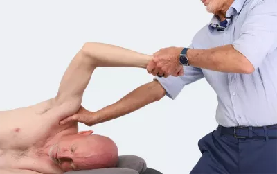 Massage therapist Erik Dalton grips a sidelying client's right arm while pushing against the client's shoulder.