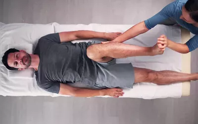 Overhead view of a massage therapist working on a male client's leg on a table.