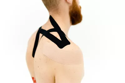 A man with a beard and short hair with kinesio tape across his neck and lats.