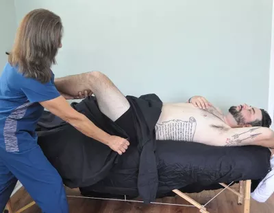 A massage therapist demonstrates draping over a leg on a client supine on a table.