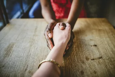 Two people grasping hands in a comforting manner.