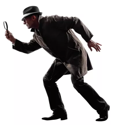 Detective in a coat and hat with a magnifying glass tiptoeing.