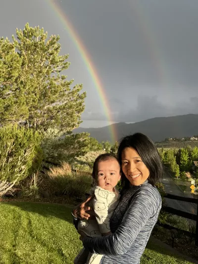 A photo of Kei Yumoto standing outside with a cgild under a rainbow.