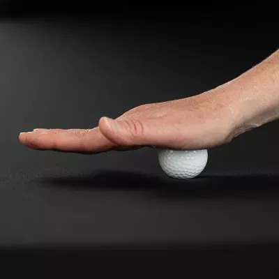 Demonstration of massaging the palm with a golf ball on a table.