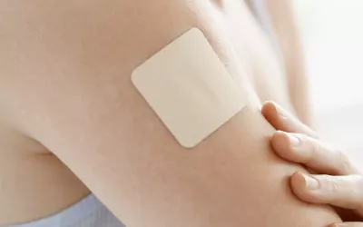 A nondescript, square medication patch is on a person's arm.