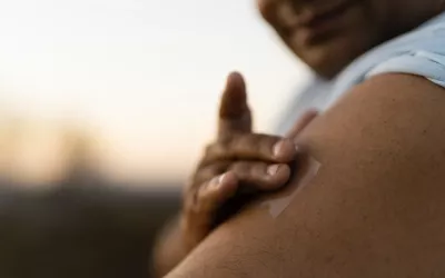 A person applies a medication patch to their left arm.