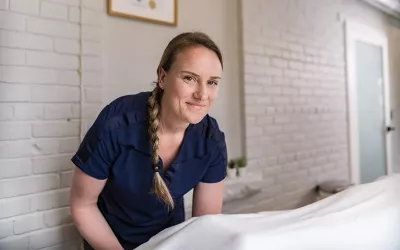 MT looking into the camera lens as she tends to sheets on a massage table.