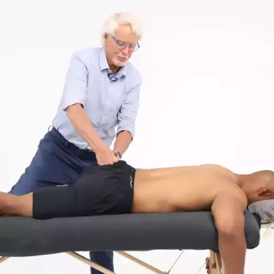 Massage therapist Erik Dalton performs a technique known as spindle-stim glutes to a male client who is prone on a table.