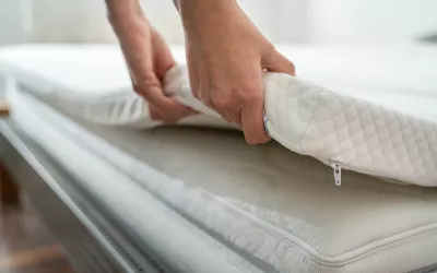 A pair of hands adjusts a thin padding on a bed. 