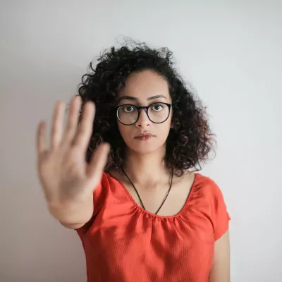 A woman with glasses stands with her arm outstretched in a "stop" gesture.