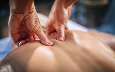 Close up image of a massage therapist's hands kneading the upper back of a client.