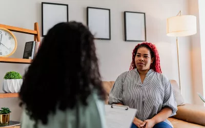 A woman client listens to her therapist who holds a clipboard with information during a session.