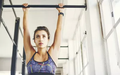 A woman hangs from a chin-up bar.