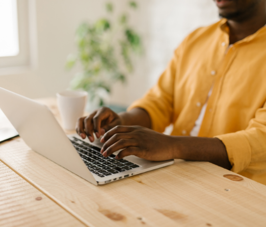 a man in a yellow shirt types on a laptop