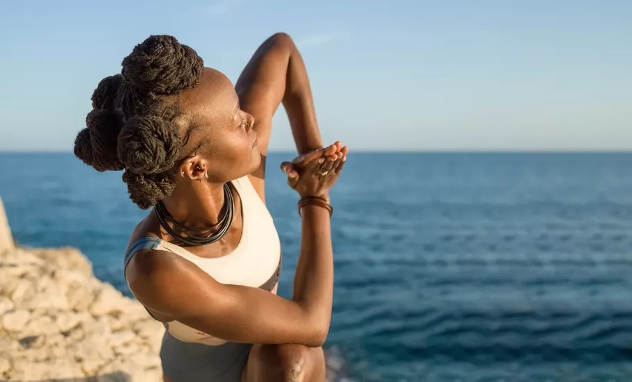 A woman twists and stretches on a cliff near the sea.