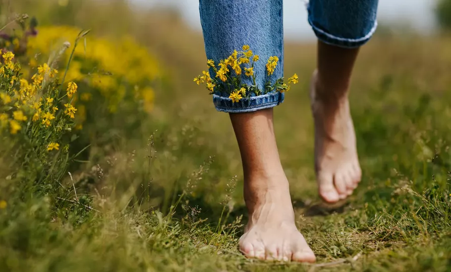 A pair of feet walk through a field with little flowers tucked into the cuff of their jeans.