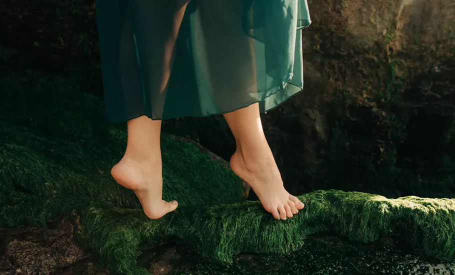 A dancer on their toes walks on a mossy bed.