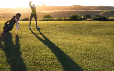 A golfer starts his backswing as the sun sets behind him.