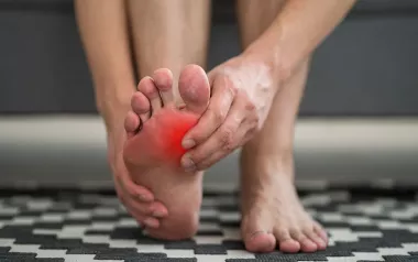 A person massages their own foot, which appears to be in pain via red coloring near their big toe. 