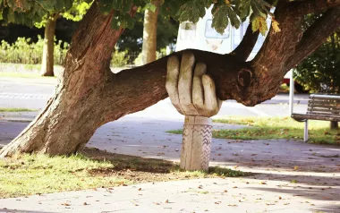 A statue of an arm and hand hold up a large branch of a tree.