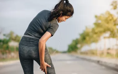 A woman grabs the back of her right leg which is causing her pain.
