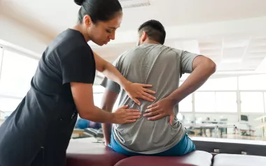 A female therapist does an assessment on a male client's back.