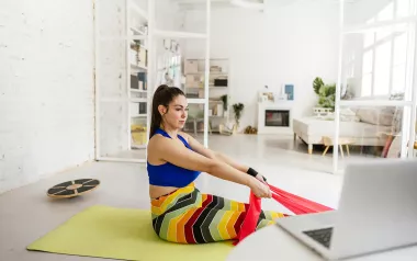 a woman on a yoga mat uses a stretching band on her feet as she follows an online class.