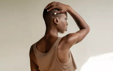 a Black woman in a tank top with a buzz cut holds her arm over her head, rotating her scapula.