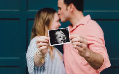 a male and female couple kiss while they hold up an ultrasound photo of a baby.