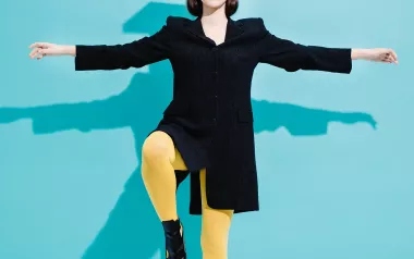 a woman in black and yellow clothes balances a book on her head while standing on one foot.