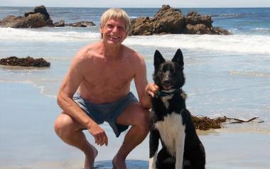 Art Riggs on Carmel Beach in Monterey County, California, smiling with his dog.