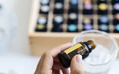 a large selection of small bottles of essential oils, with one being added to a cup.