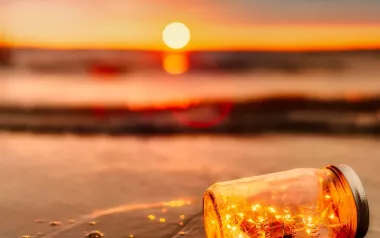 yellow string lights in a jar, floating on a beach at sunset.