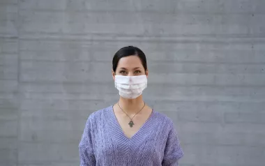 a woman in a purple sweater wears a disposable face mask.