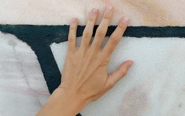 a hand with the palm splayed up against a painted abstract wall.